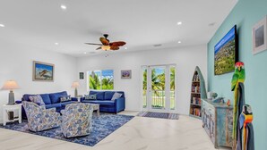 A living room with a blue sofa set, a ceiling fan, and a bookshelf. - P98 - 75ft dock with shore power, 4 bed, 4 bath home w/private pool in Sombrero Beach Neighborhood. (Marathon)