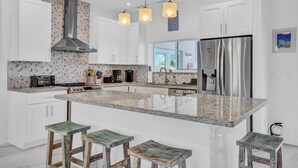 A modern kitchen with white cabinets, a stainless steel refrigerator, a central island with stools, and pendant lighting. - P98 - 75ft dock with shore power, 4 bed, 4 bath home w/private pool in Sombrero Beach Neighborhood. (Marathon)