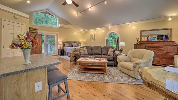 A spacious living room with a large sofa, a coffee table, and a dining area. There is a ceiling fan, a large window, and a view of the outdoors. - Quiet Studio Escape ~ 2 Mi to Blue Ridge Parkway! (West Jefferson)