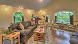 A spacious living room with a brown leather couch, a wooden coffee table, and a round table with chairs. There are large windows with curtains, a fireplace, and a chandelier. - Quiet Studio Escape ~ 2 Mi to Blue Ridge Parkway! (West Jefferson)