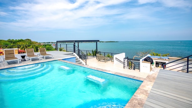 A rooftop pool with clear blue water, surrounded by lounge chairs and a wooden deck.