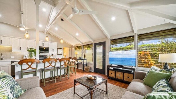 A spacious living area with a kitchen, dining set, and a large window with a view of the ocean. - Beautifully Furnish Kaanapali Cottage near Beach - International Colony Club 13 (Lahaina)