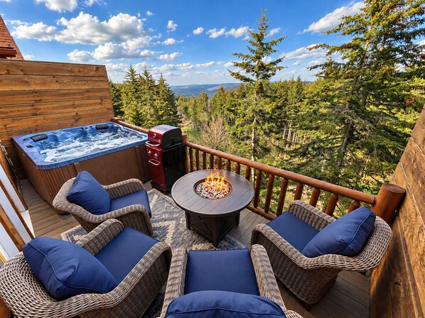 An outdoor deck with a hot tub, barbecue grill, and a fire pit surrounded by wicker furniture.