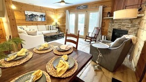 A cozy cabin-style room with a dining area set for four, a fireplace, and a living area with a sofa and armchairs. - Ski In/Out, Watch Slope frm Hot Tub, 6BR, 3 Kings, PS5, Tesla, Rec Rm-Loggers 12 (Snowshoe)