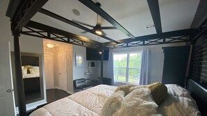 Une chambre à coucher avec un grand lit, un ventilateur de plafond, une fenêtre avec des rideaux et une porte donnant sur une autre pièce.