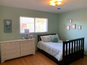 Une chambre à coucher avec un lit, une commode, une fenêtre et des éléments décoratifs sur les murs.