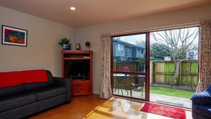 A living room with a sofa, TV, and a sliding glass door leading to a backyard. - Spacious 1 bedroom Cottage (Kaikoura)