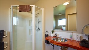 A bathroom with a glass-enclosed shower, a wooden vanity with a sink, and a mirror above the vanity. - Spacious 1 bedroom Cottage (Kaikoura)