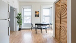 A dining area with a table and chairs, a potted plant, and a painting on the wall.