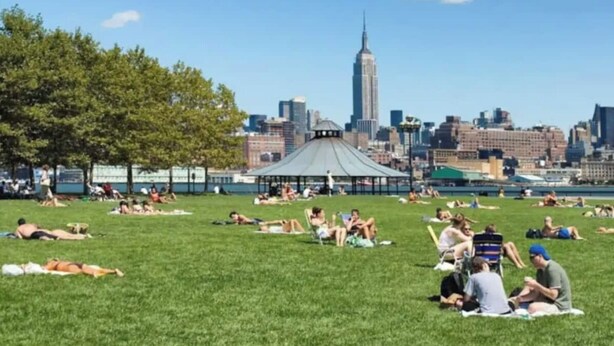 A park with people sunbathing and sitting on blankets, a gazebo, and the Empire State Building in the background.