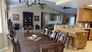 A spacious dining area with a long wooden table and chairs, a kitchen with wooden cabinets, and a ceiling fan.
