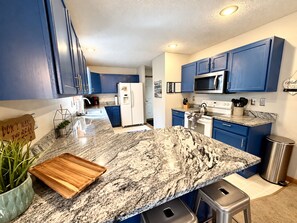 A modern kitchen with blue cabinets, granite countertops, a stainless steel refrigerator, and a microwave. - Lake Front Lodge Hot tub fire pit Kayak (Blakeslee)