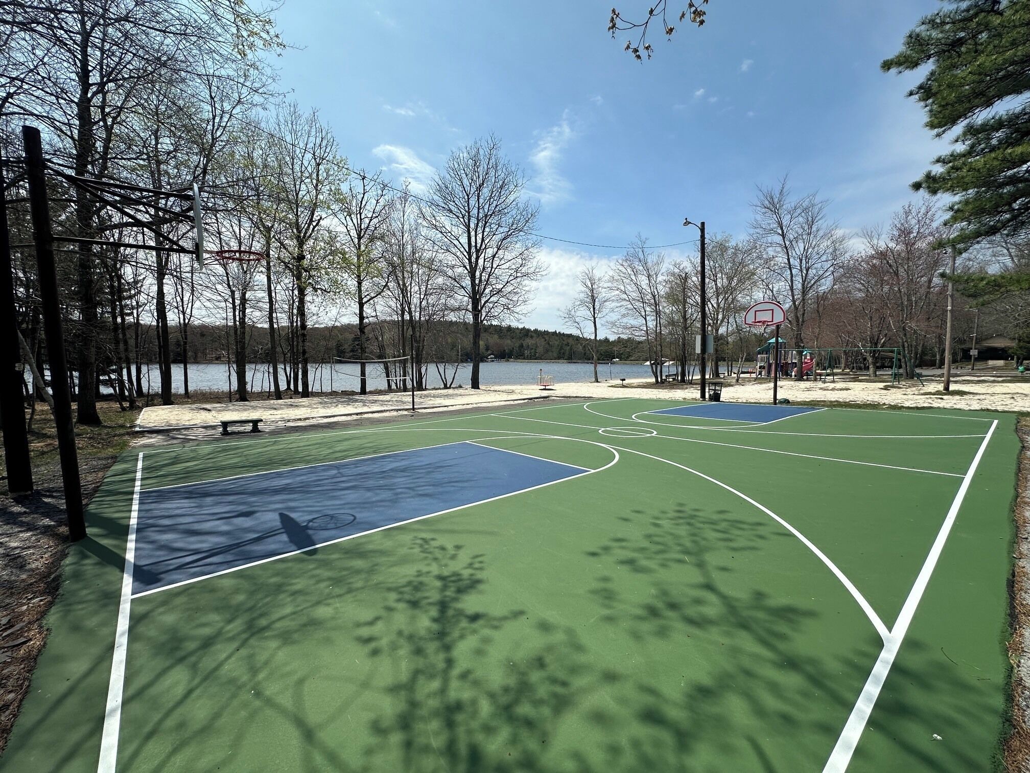 An outdoor basketball court with a net, surrounded by trees and a body of water.
