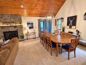 A cozy living room with a fireplace, a dining area with a wooden table and chairs, and a stone wall. - Lake Front Lodge Hot tub fire pit Kayak (Blakeslee)