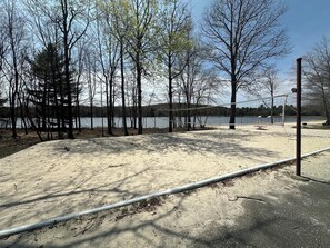 Une plage de sable avec un filet de volley-ball, des arbres et une étendue d’eau en arrière-plan.