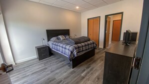 Een slaapkamer met een bed, een nachtkastje, een bureau met een computer en twee deuren.