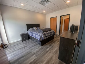 A bedroom with a bed, a nightstand, a desk with a computer, and two doors.