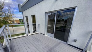 Een modern gebouw met een houten terras, grote schuifpuien en een metalen hekwerk.