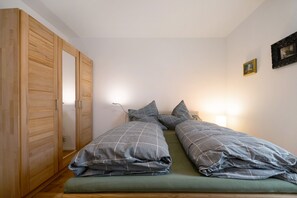 A bedroom with two beds, a wooden wardrobe, and a wall-mounted lamp.
