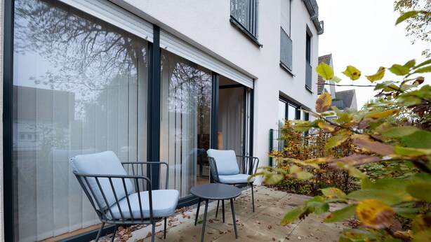 A patio with two chairs and a small table, a large window, and a view of a building. - Holiday Apartment at the "Gustavsburg" Castle with Wi-Fi & Terrace (Homburg)