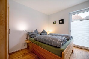 Un dormitorio con cama de madera, ropa de cama verde y una ventana con persianas.