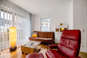 Una sala de estar moderna con un sofá de cuero, una silla roja, una mesa de centro y una lámpara.