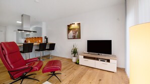 A modern living room with a TV, red leather chairs, a wooden cabinet, and a dining area with chairs and a table. - Holiday Apartment at the "Gustavsburg" Castle with Wi-Fi & Terrace (Homburg)