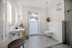 Un baño moderno con lavamanos, inodoro y zona de ducha blancos.