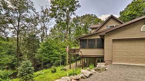 Ein zweigeschossiges Haus mit Garage, eingebettet in eine natürliche Landschaft mit Bäumen und einem kleinen Bach.