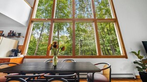 A dining area with a large window, a table, chairs, and a vase with flowers.