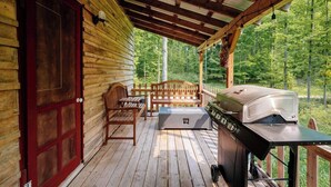 A wooden deck with a grill and seating area, overlooking a forested area.