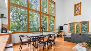 A spacious living area with large windows, a dining table, and a gray sofa.