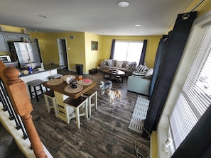 Une cuisine moderne avec un coin repas, un salon avec un canapé et un chien, et un escalier.