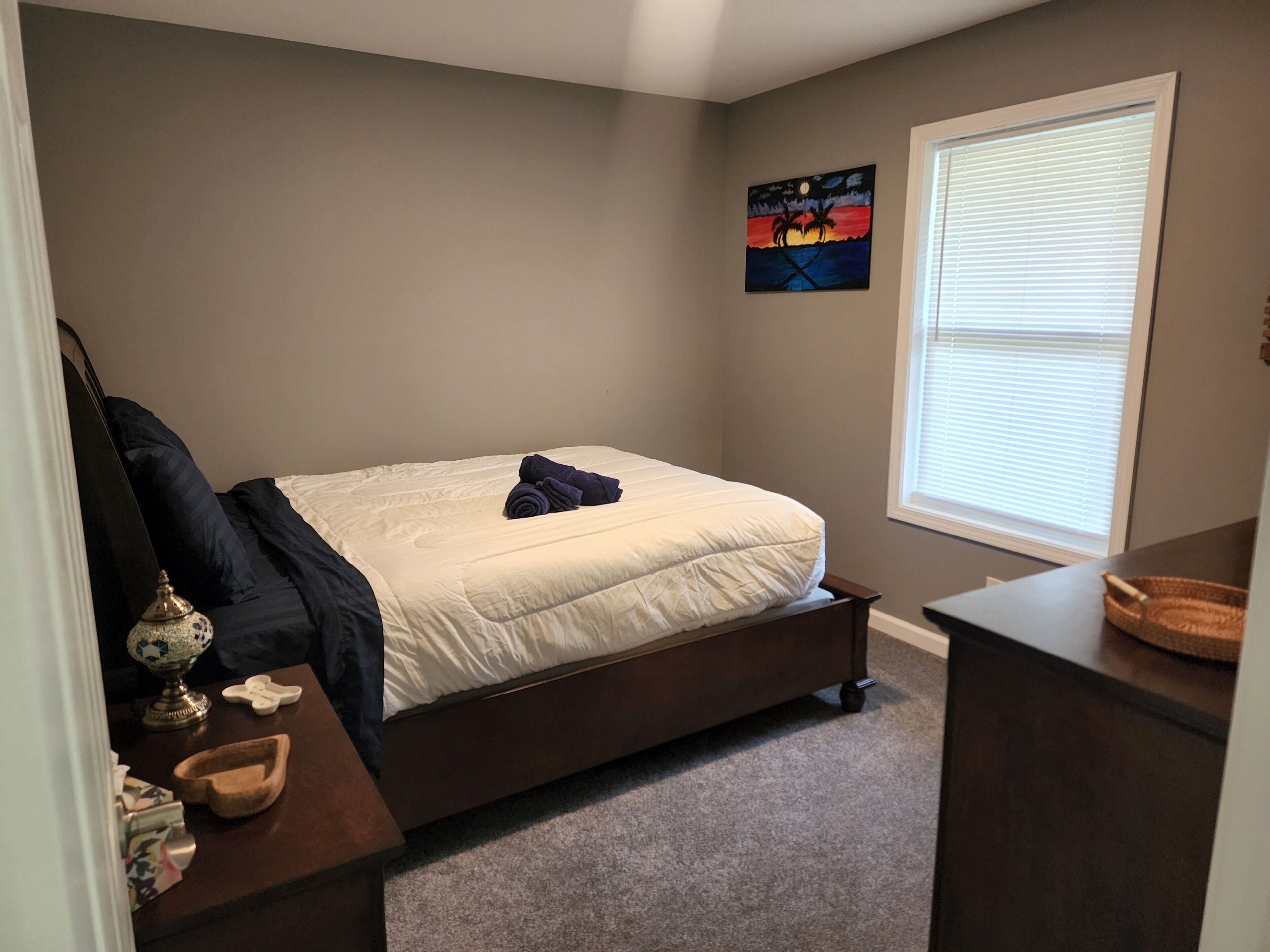 A bedroom with a bed, a nightstand, a lamp, and a painting on the wall.