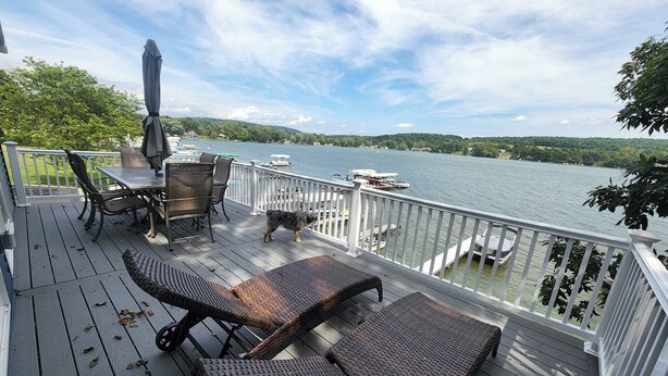 Une terrasse dotée de meubles en osier, d’une table et de chaises, offrant une vue sur un lac où naviguent des bateaux.