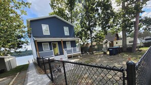 Une maison avec une véranda, une cour clôturée et un plan d’eau en arrière-plan.
