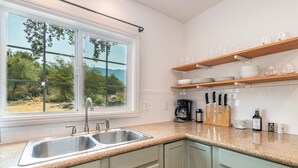 Una cocina con un lavamanos doble, repisas de madera sobre la encimera y vista a la vegetación exterior.