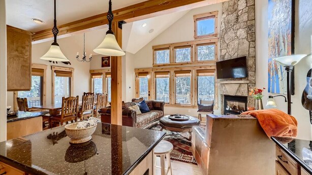 A spacious living area with a large island, wooden beams, stone walls, and multiple windows. - Beautiful 3 bedroom with private hot tub, walkable to town and trails (Frisco)