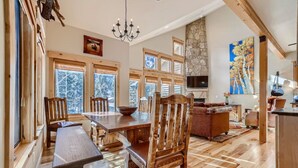 A spacious dining area with wooden furniture, large windows, and a stone fireplace. - Beautiful 3 bedroom with private hot tub, walkable to town and trails (Frisco)