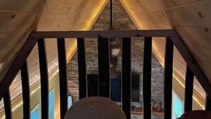 A wooden attic room with a sloped ceiling, a large round bean bag chair, and a view of a stone fireplace through a window.