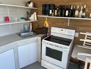Une cuisine avec un four blanc, un évier et un plan de travail. On peut voir des bouteilles de vin sur une étagère au-dessus du plan de travail.