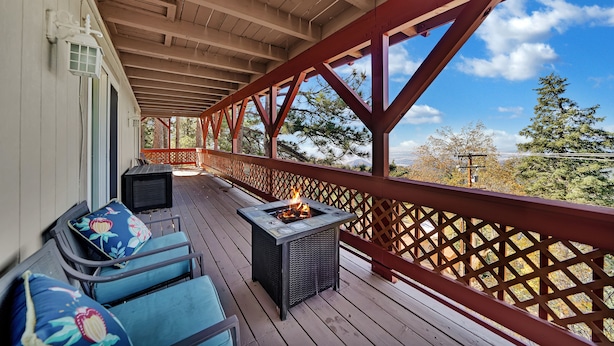 A covered deck with a fire pit, outdoor seating, and a view of trees and mountains. - 3-bedroom cabin near Santa's Village-13 minutes from Snow Valley Mountain Resort (Running Springs)