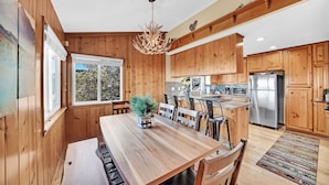 A wooden-paneled kitchen with a dining area, featuring a chandelier, wooden cabinets, and a refrigerator. - 3-bedroom cabin near Santa's Village-13 minutes from Snow Valley Mountain Resort (Running Springs)