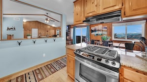 A kitchen with wooden cabinets, a stainless steel stove, and a large window offering a mountain view. - 3-bedroom cabin near Santa's Village-13 minutes from Snow Valley Mountain Resort (Running Springs)