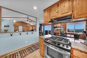 A kitchen with wooden cabinets, a stainless steel stove, and a large window offering a mountain view.