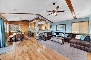 A spacious living room with a wooden floor, a ceiling fan, and a large window.