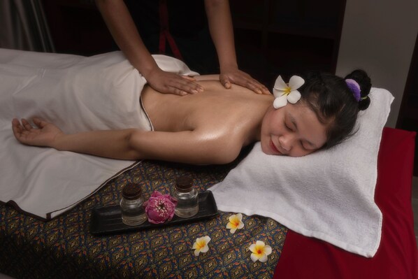 A person receiving a massage on a bed with a tray of massage oils and flowers. - Duong Chan Hotel (Phnom Penh)