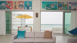 A living room with a sofa, a coffee table, and a view of the beach through large windows.