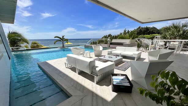 A poolside area with white outdoor furniture, a small pool, and a view of the ocean.