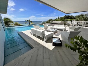 Un área junto a la piscina con mobiliario exterior blanco, una piscina pequeña y vista al océano.